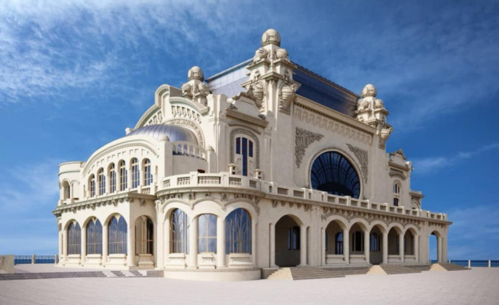 Ornate beige seaside building with arched windows and domed roof, set on a wide plaza against a blue sky and ocean backdrop